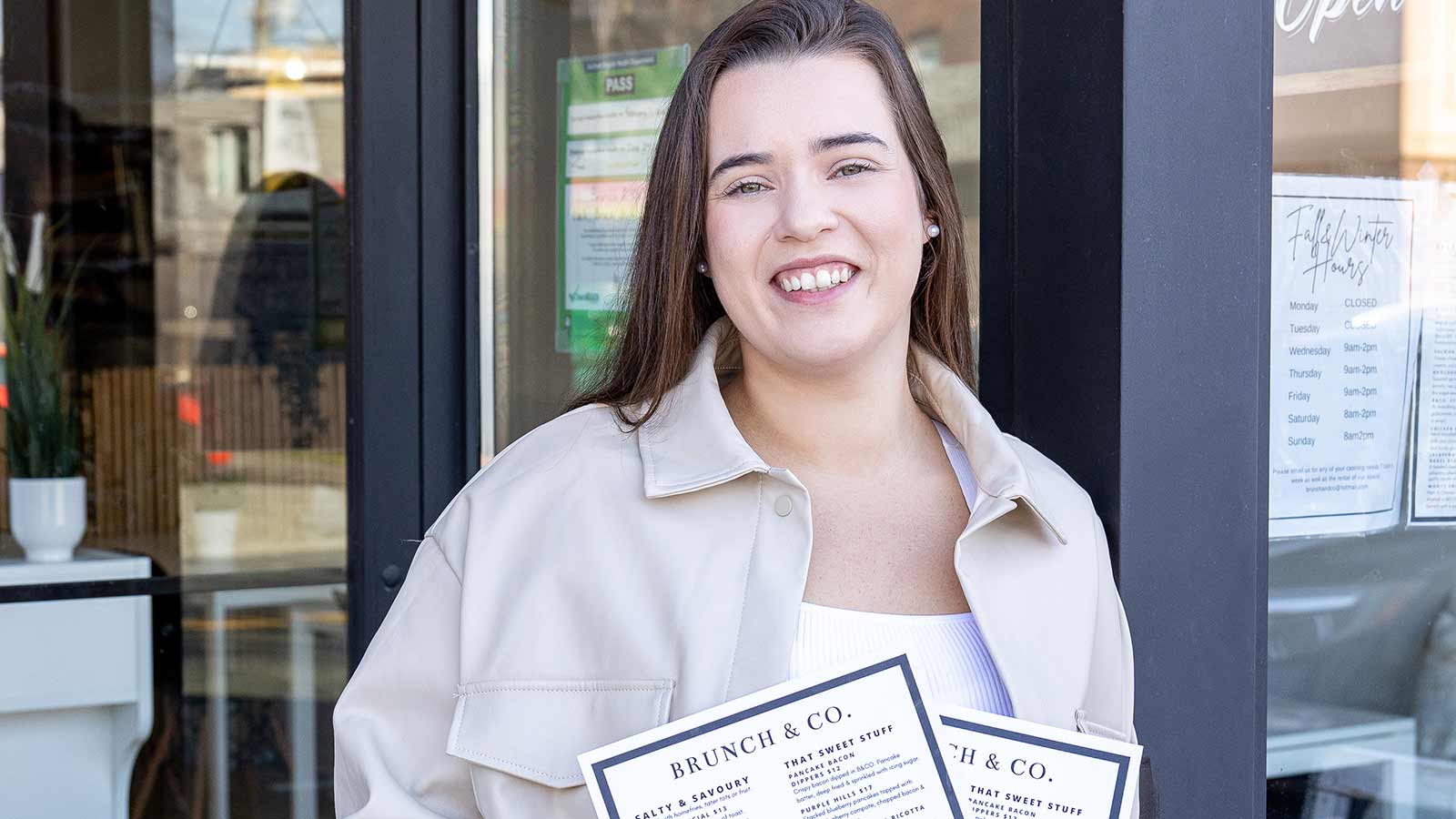 Owner Sarah Pascoal smiling and holding menus outside of restaurant