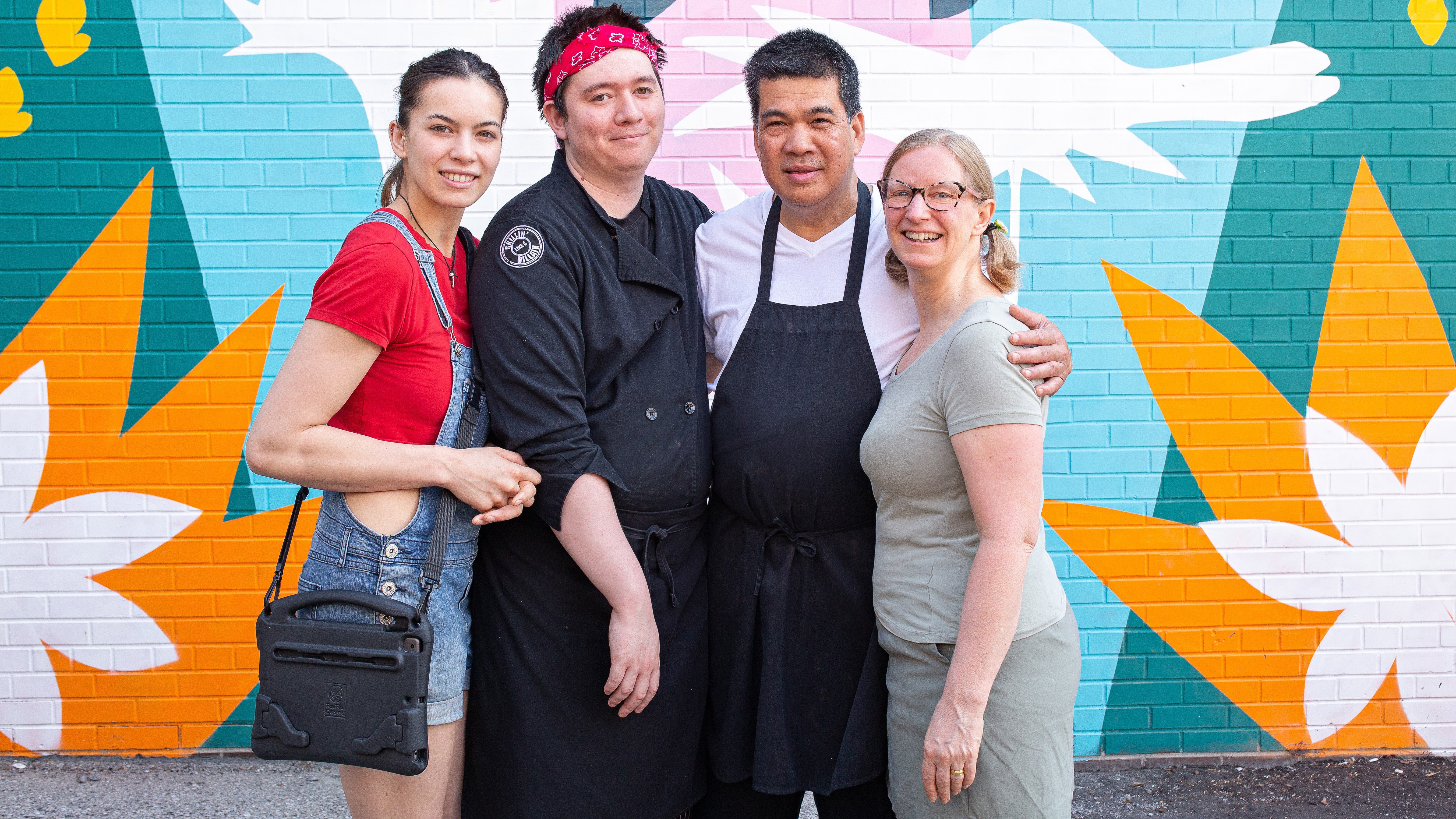 Alison and Noel Galvan, owners of the Food and Art Cafe, accompanied by their adult children, Phoebe and James, standing in front of a vibrant mural