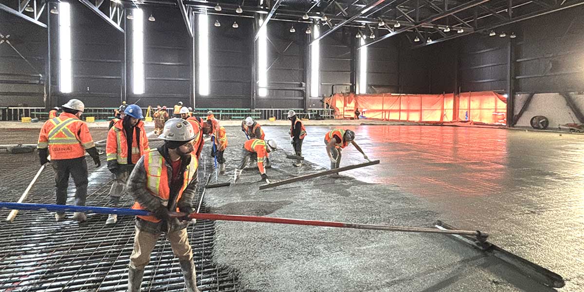 Workers pouring a cement arena pad