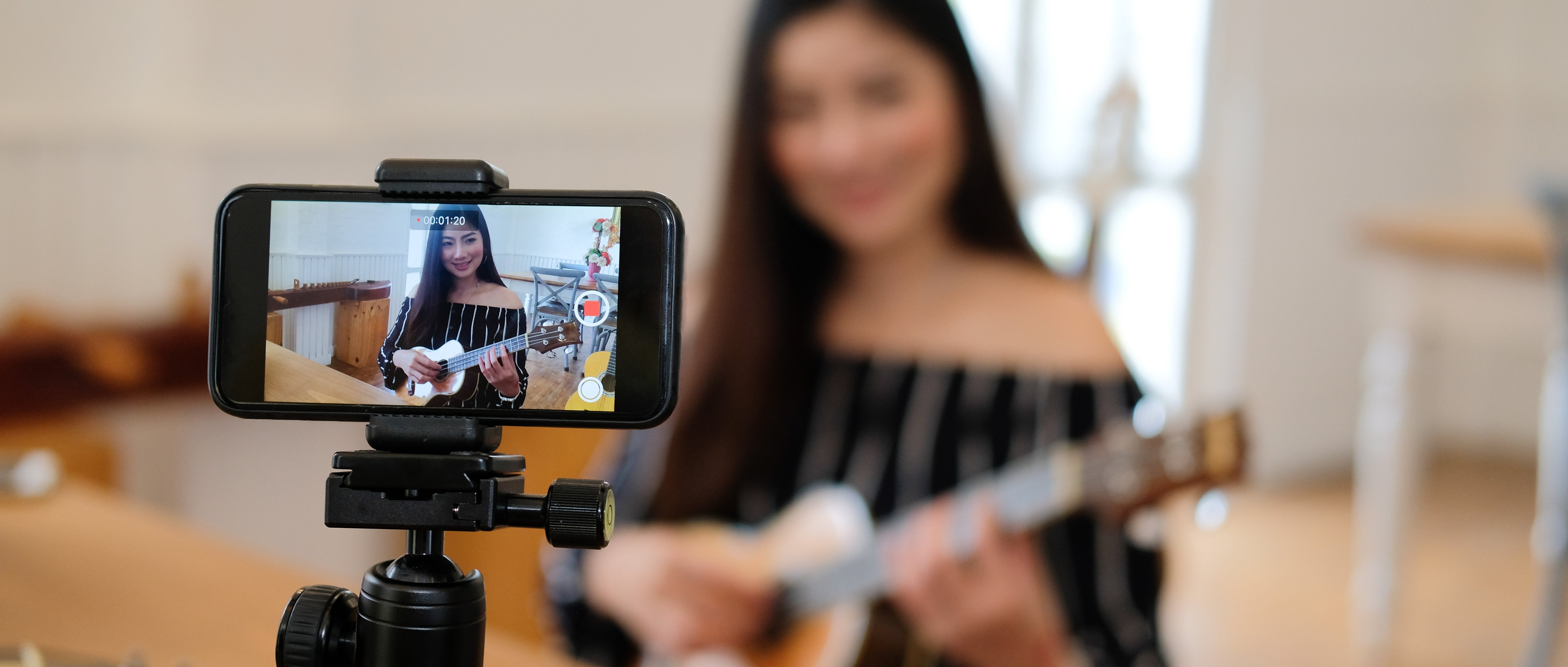 Woman recording herself playing guitar with a smartphone