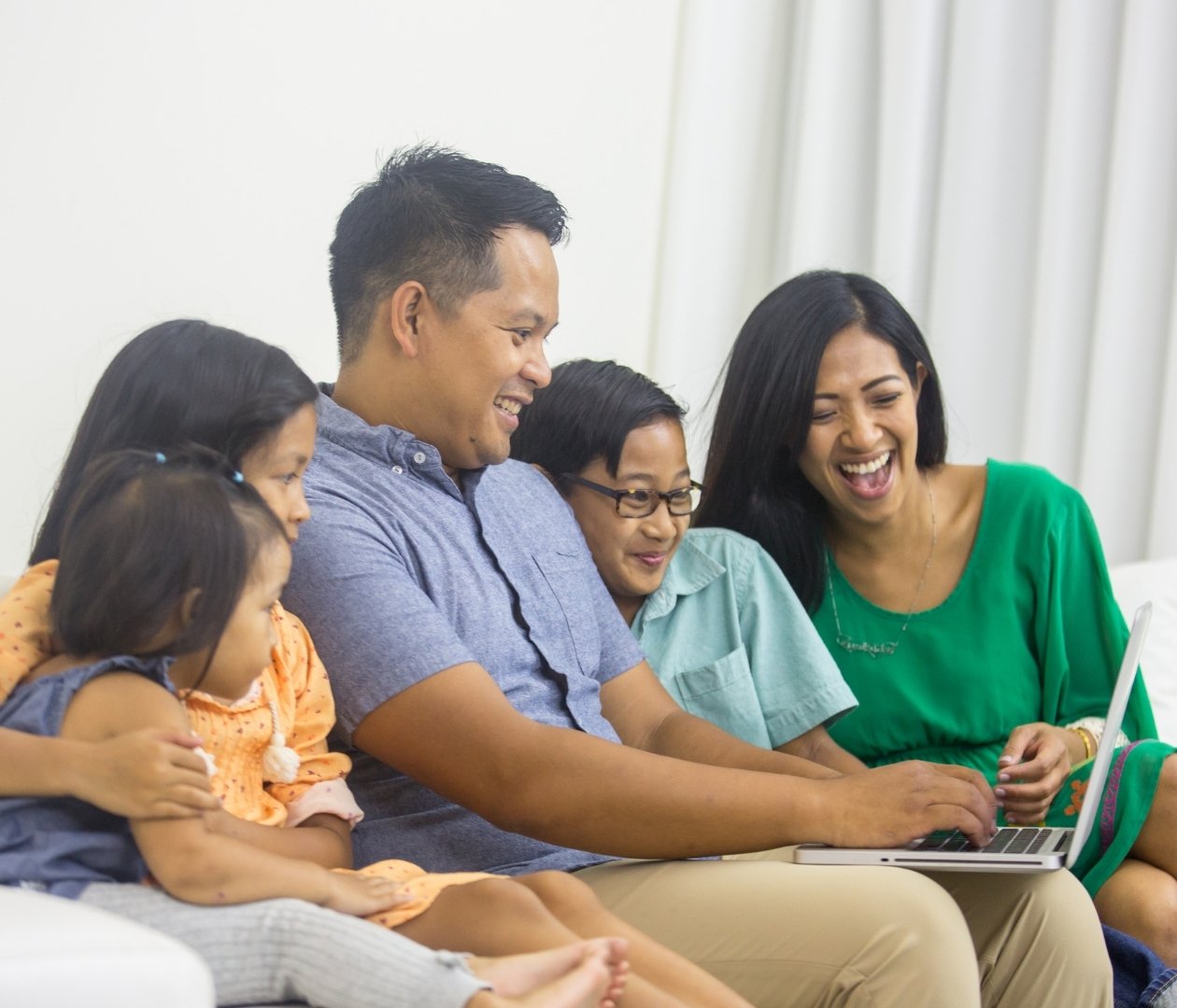 Family of five sitting on the couch using laptop