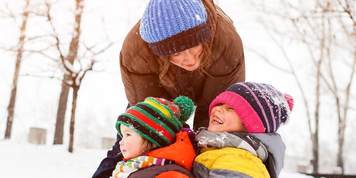 Parent pushing two children on a sled in winter