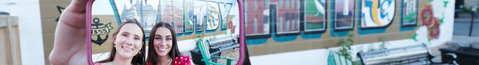 Women holding phone and taking selfie in front of mural