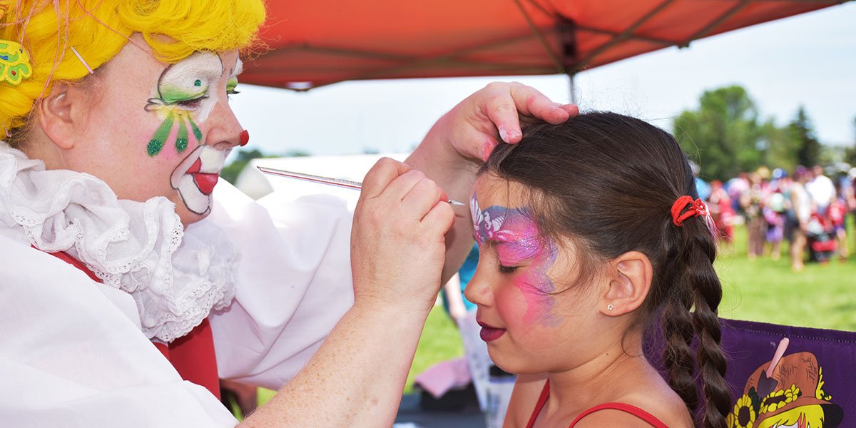 Child having face painted by a person in a clown costume