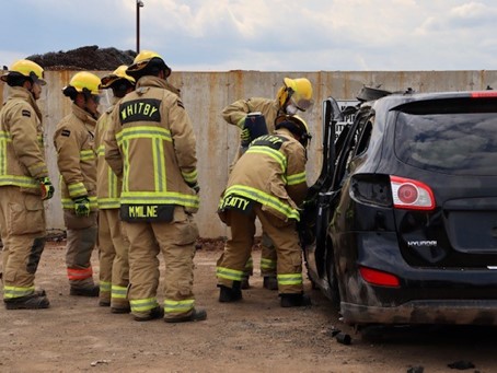 Firefighters and recruits using the jaws of life to remove the driver's side door from the vehicle.