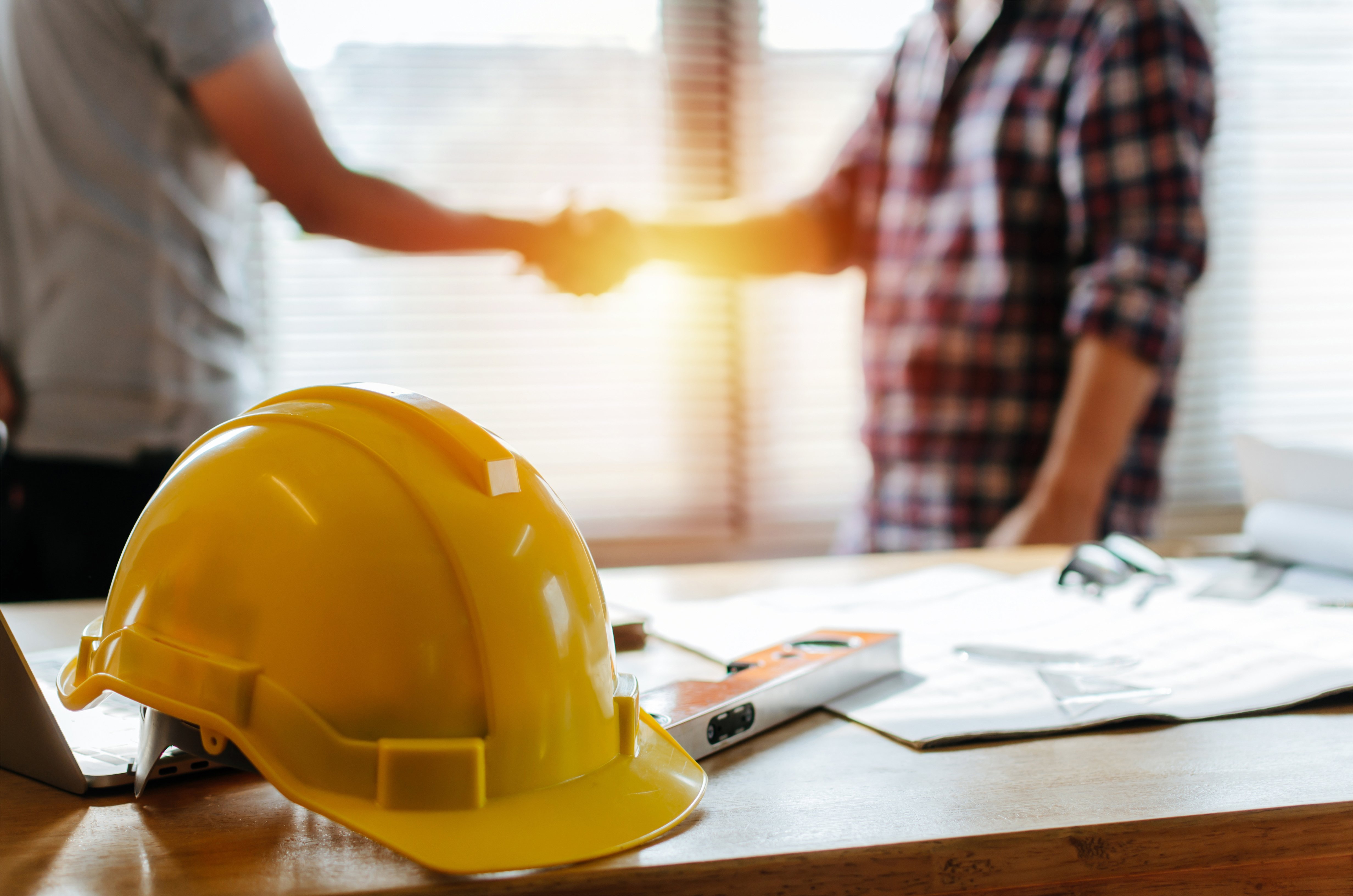 a yellow hardhat sitting on a desk with people shaking hands in the background