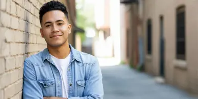 Youth leaning against brick wall in alley and smiling 